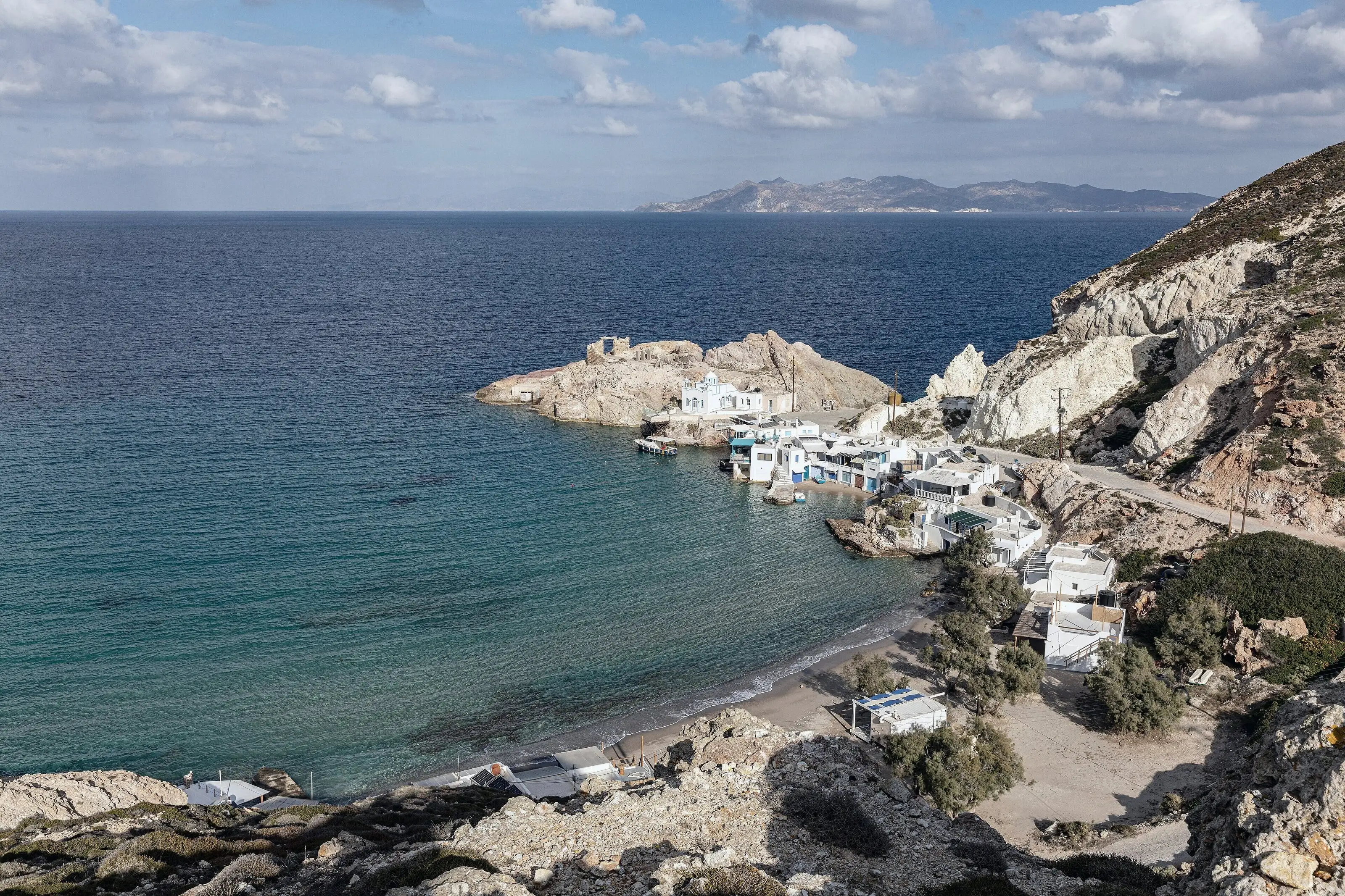 Ο κόλπος του Φυροπόταμου από τον δρόμο: τα σύρματα, το εκκλησάκι στον βράχο και τα καθαρά νερά του όρμου