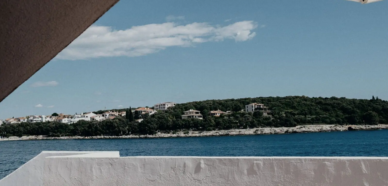 Θέα από βεράντα σε ήσυχο κόλπο, με σπίτια στην απέναντι ακτή